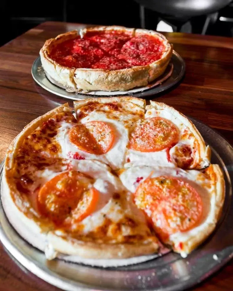 Two pizzas on metal trays, one with pepperoni and the other with cheese and pepper slices, on a wooden table.